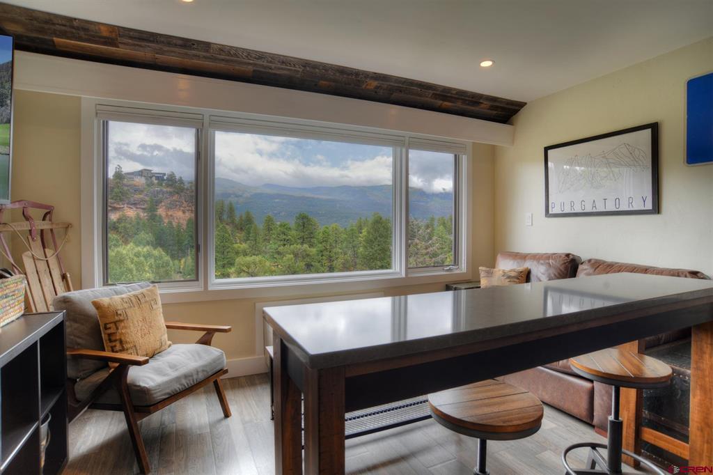 Furnished living area with a dark counter and stools, overlooking forested mountains through wide windows.