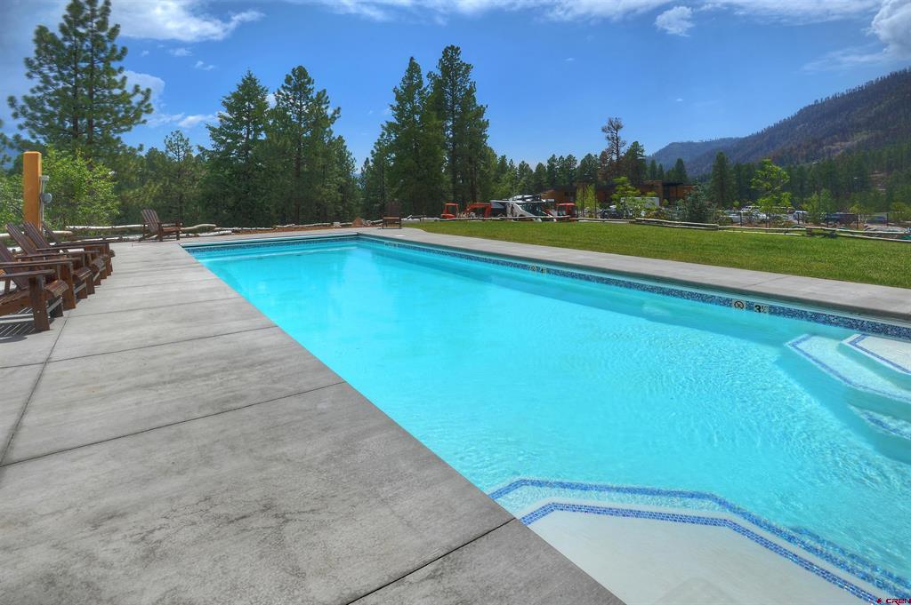 Outdoor swimming pool with a broad concrete deck, evergreen trees, and a mountain view.