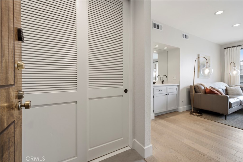 Living room and entry with louvered doors, leather sofa, and adjacent vanity.