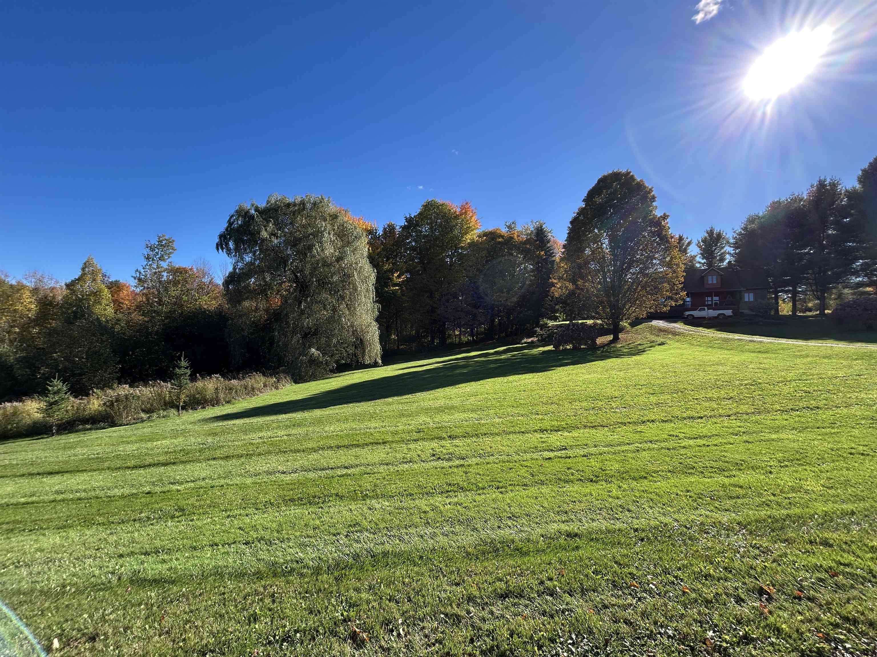 Sloping green lawn and autumn trees leading to a house set back at the right.