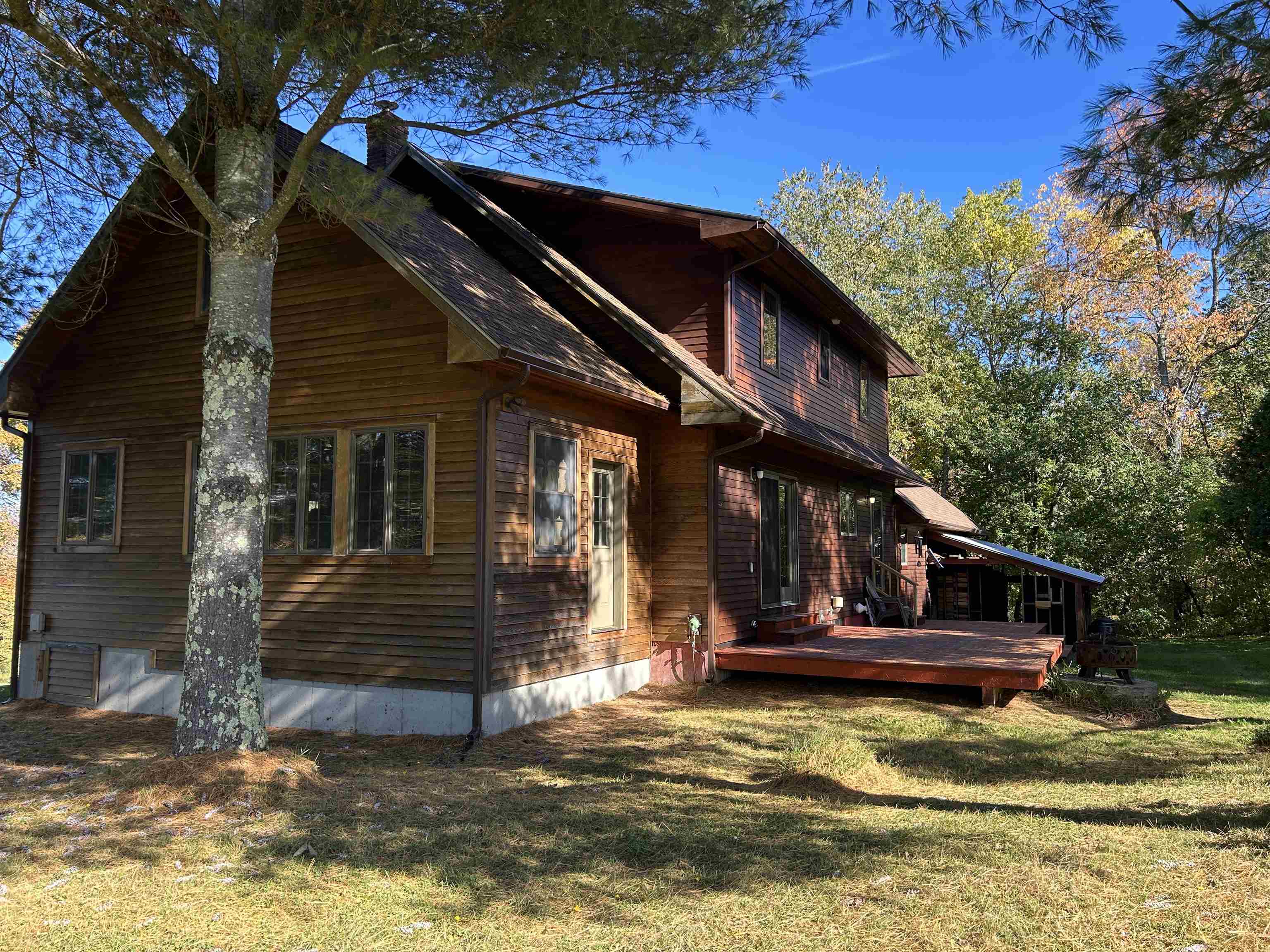 Wood-sided two-story home with a raised deck beneath mature trees.