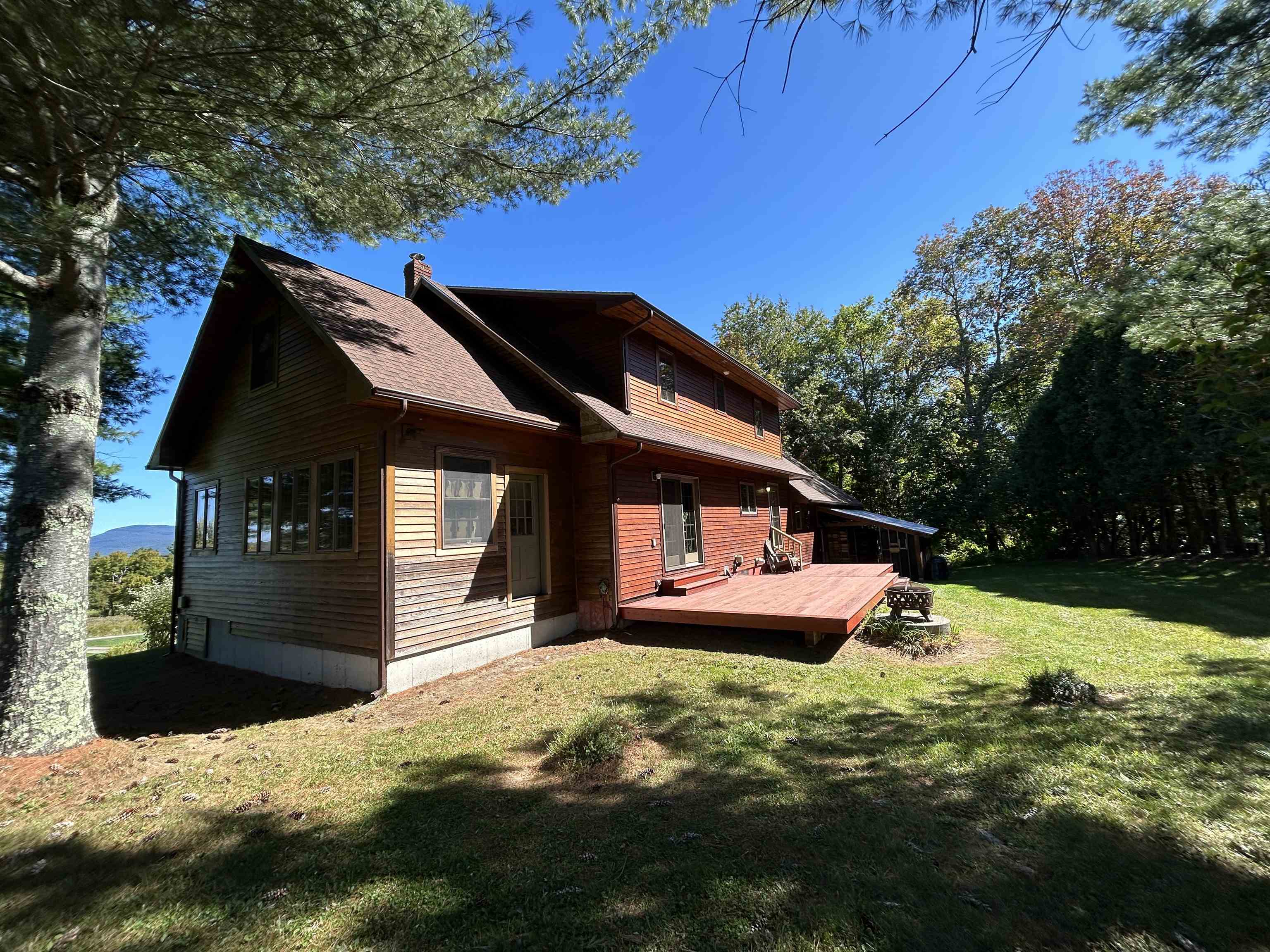 Wood-sided two-story home with a broad red deck, wooded yard, and distant mountain view.