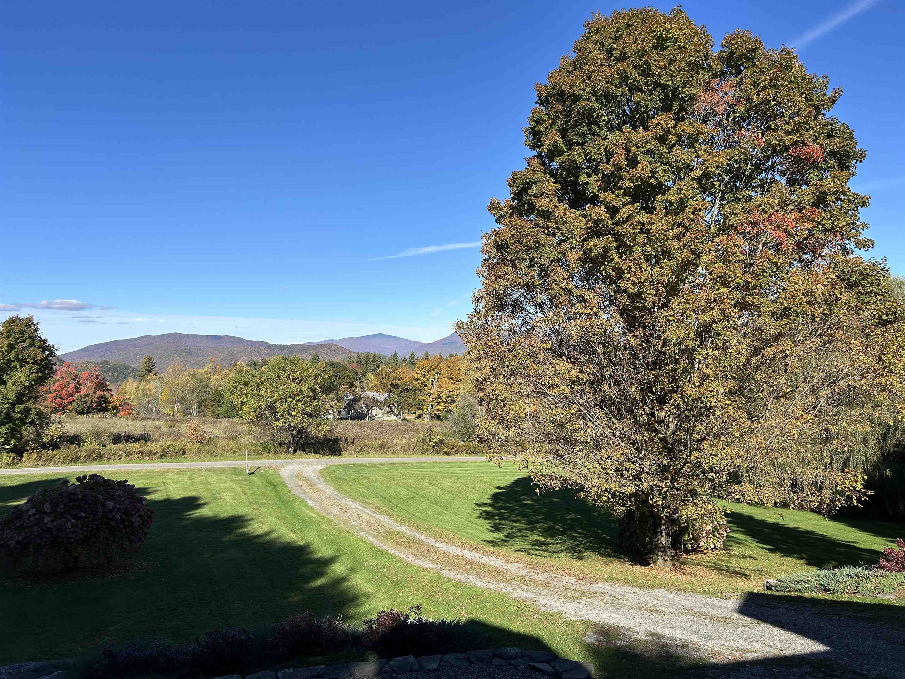 Landscaped lawn and curving gravel driveway framed by autumn trees, with mountains in the distance.