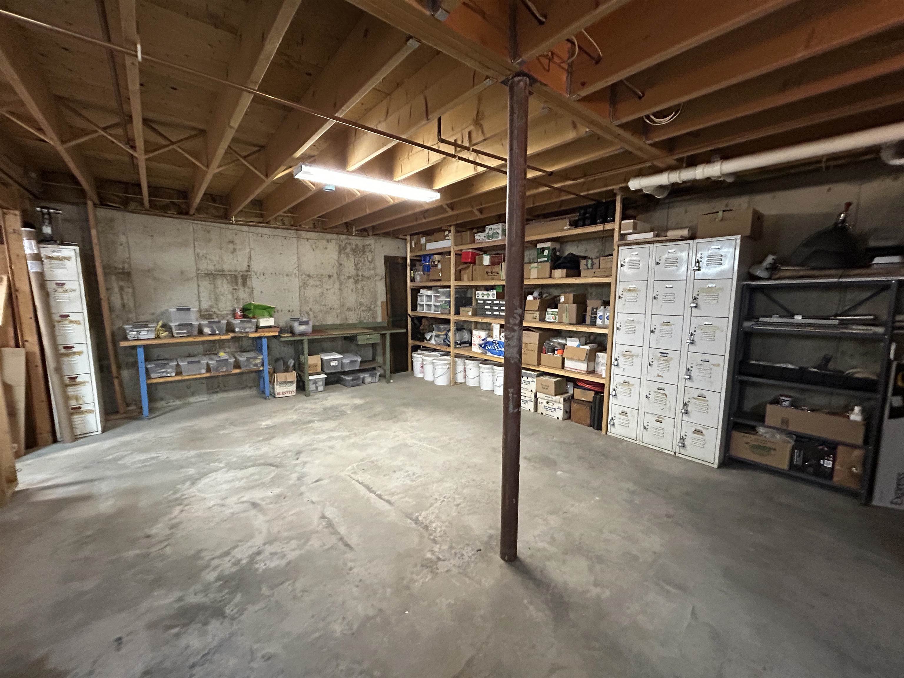 Basement storage area with exposed joists, stocked shelves, metal lockers, and a concrete floor.