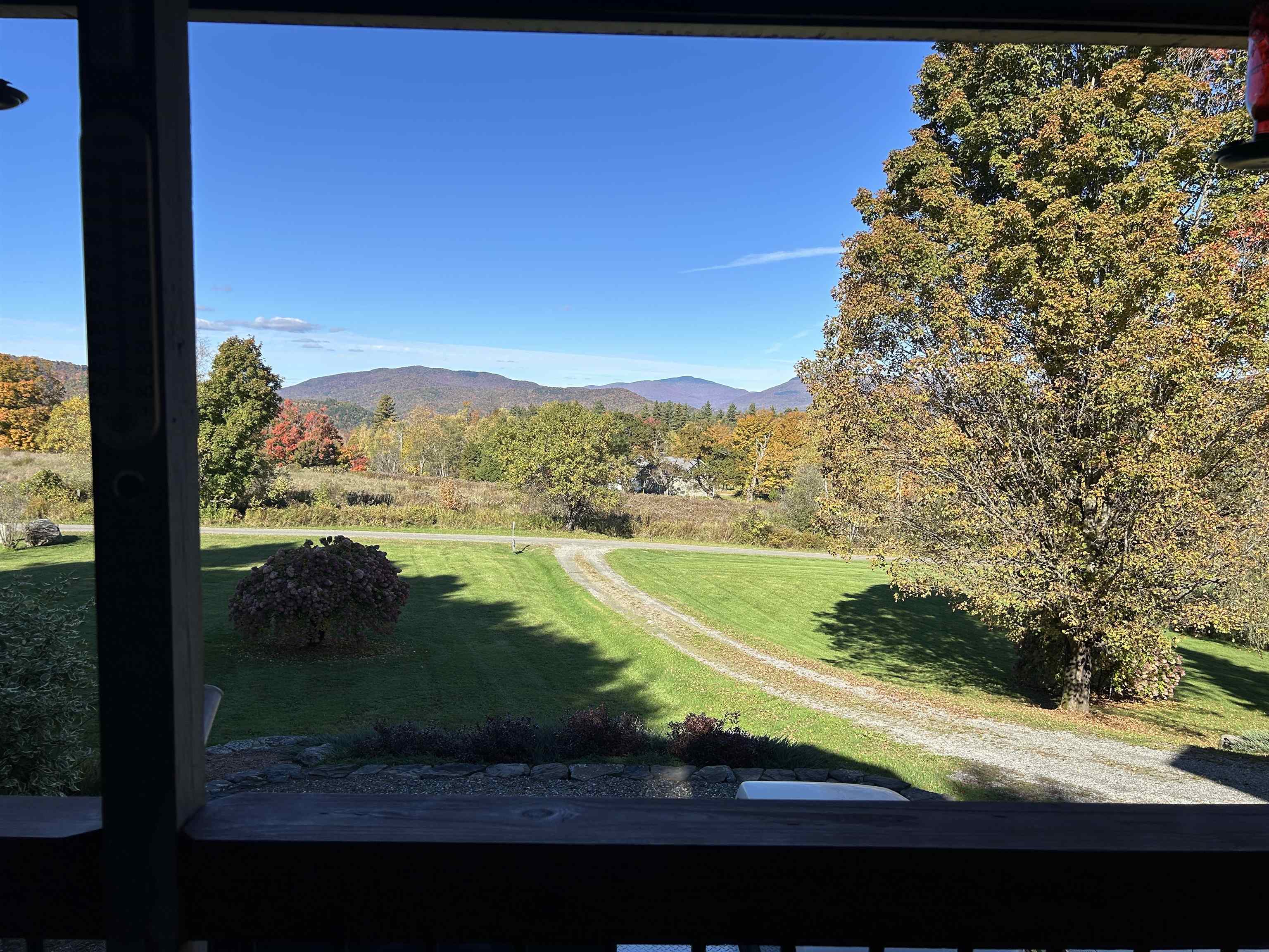 Porch view across a lawn and driveway to autumn foliage and distant mountains.