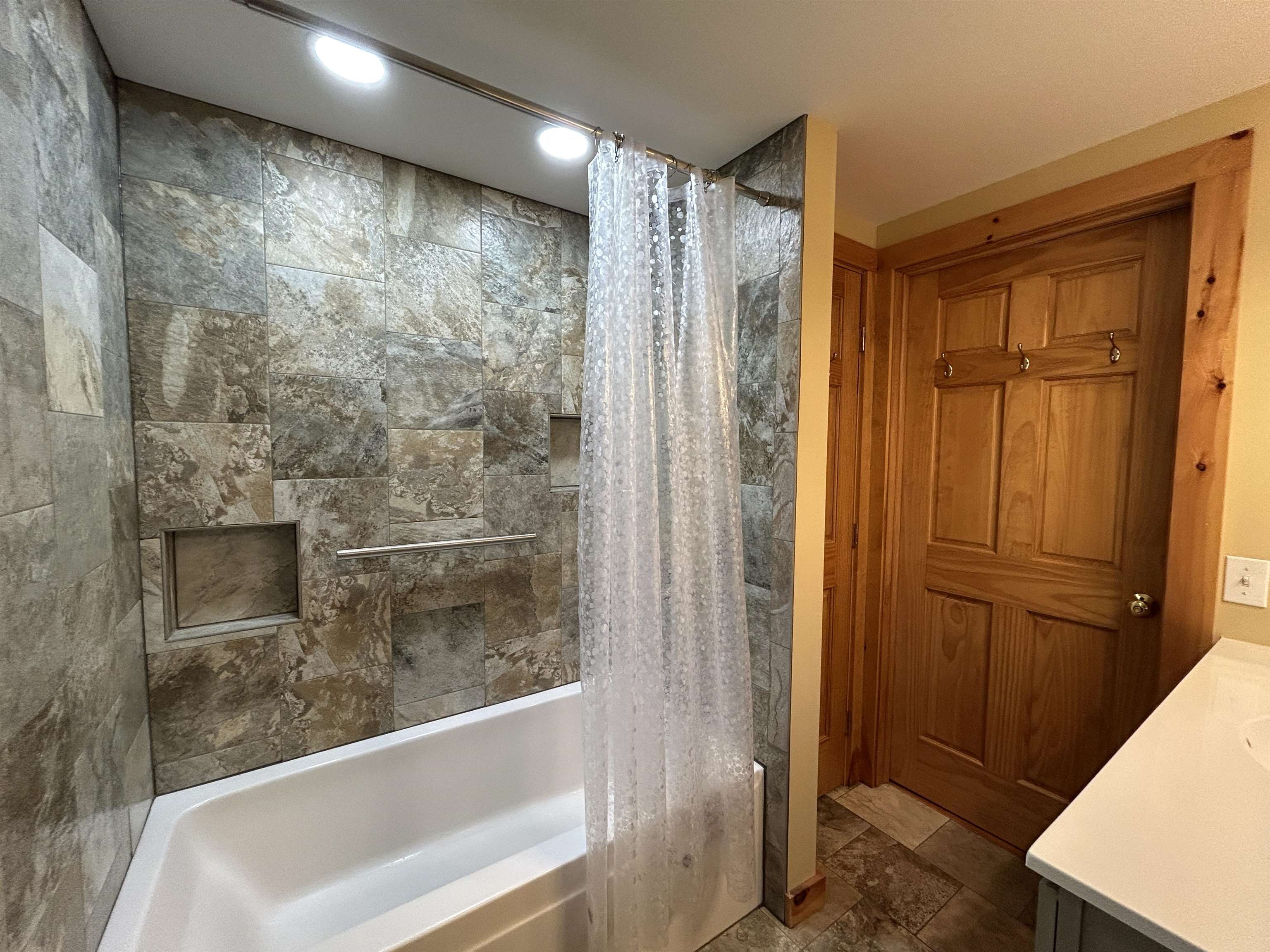 Bathroom with a stone-tiled tub and shower, built-in niches, and a paneled wooden door.