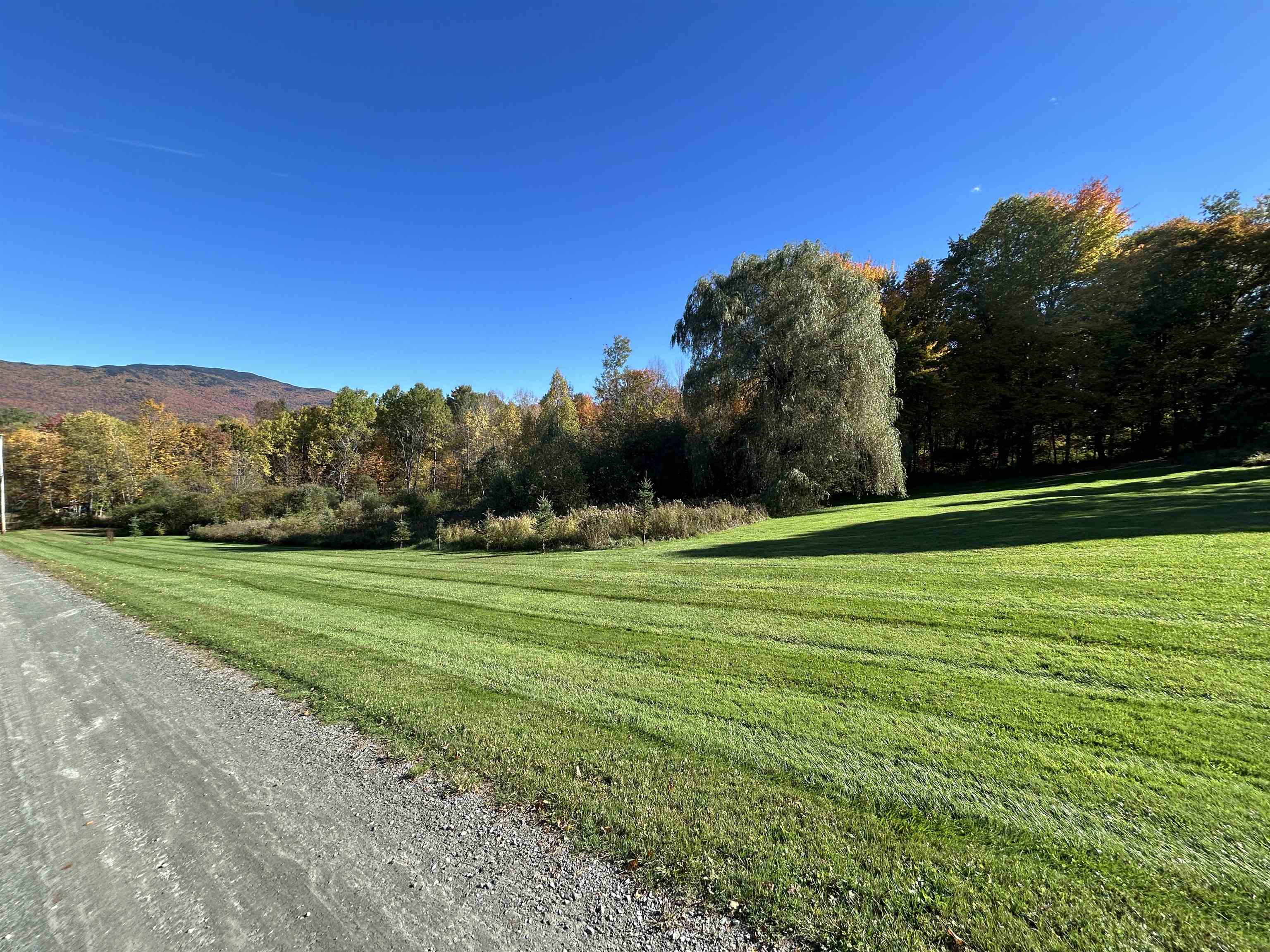 Grassy property grounds bordered by autumn trees, with a mountain ridge in the distance.