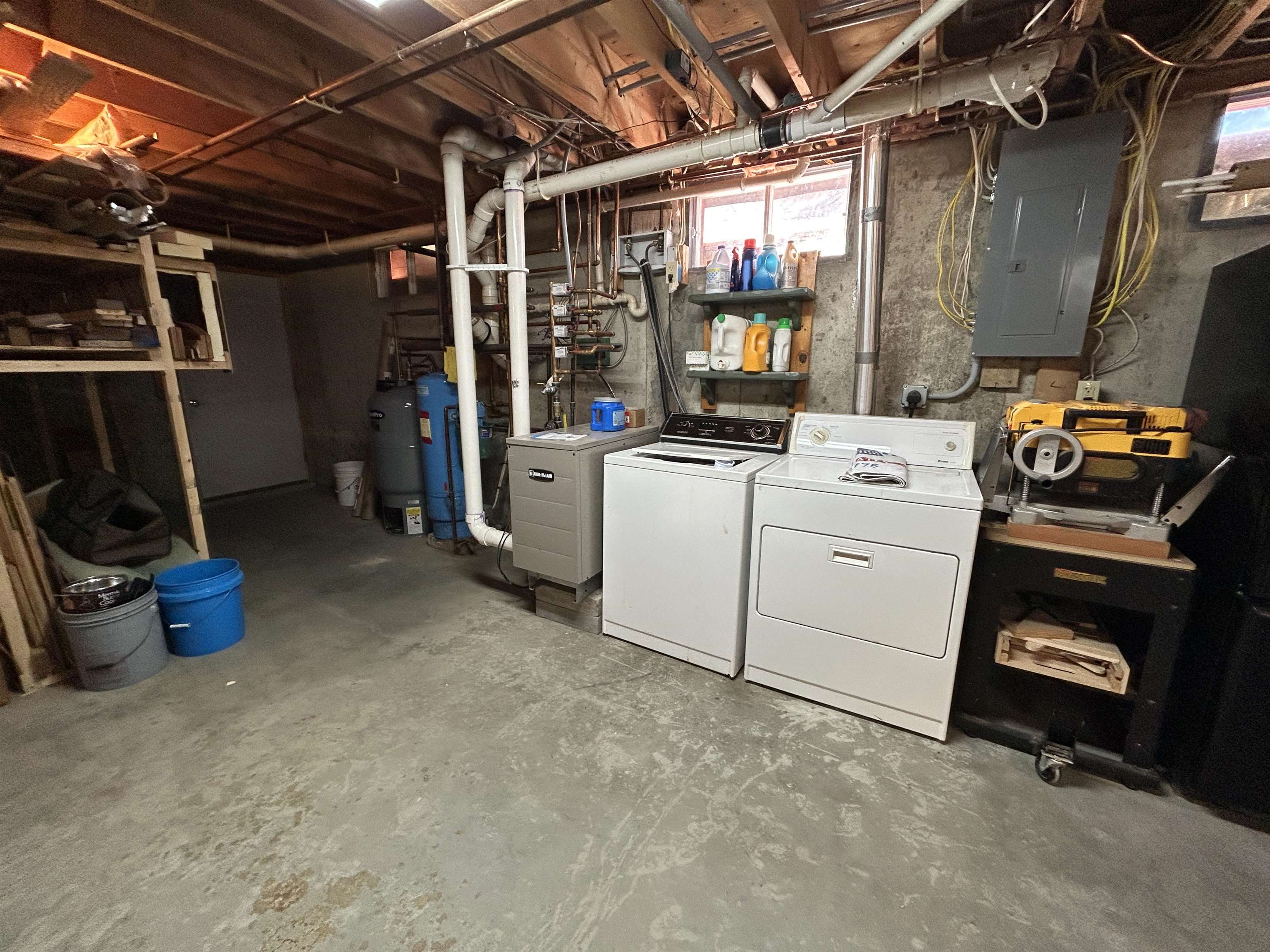 Basement laundry area with washer and dryer, water heaters, exposed pipes, and a workbench.