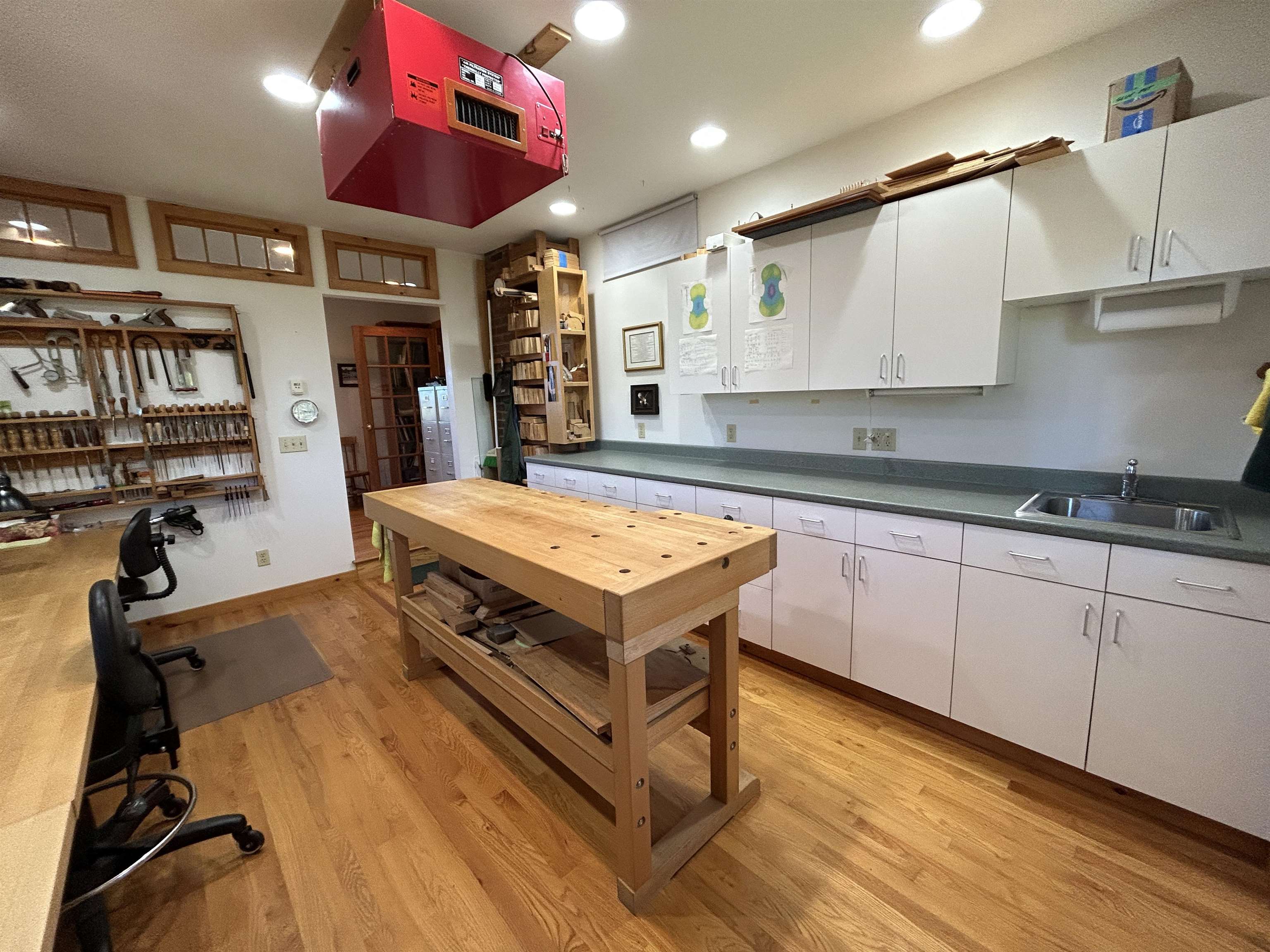 Woodworking workshop with a large central workbench, organized hand tools, and white cabinets.