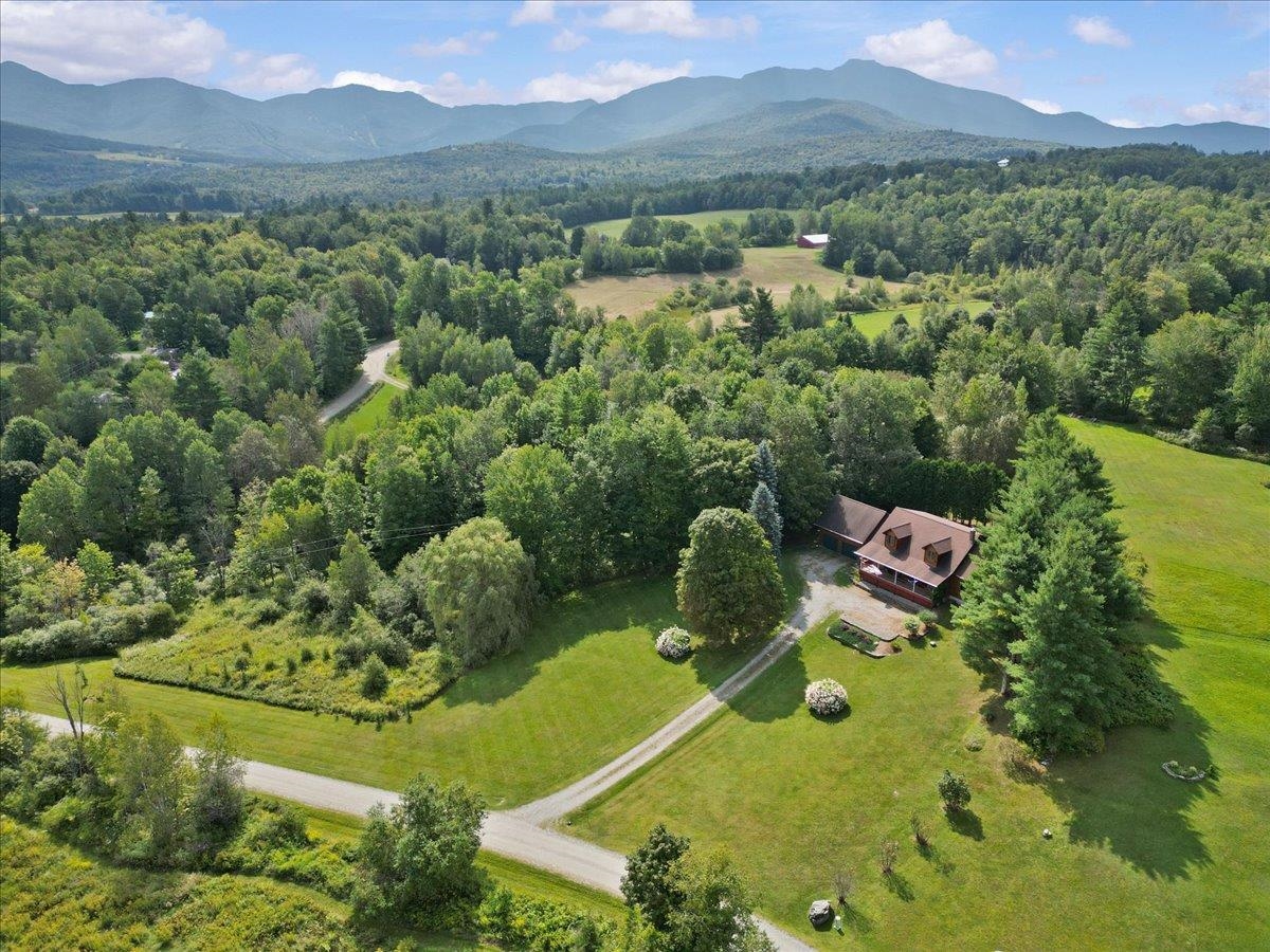Aerial view of a rural home amid lawns and trees, with mountains in the distance.
