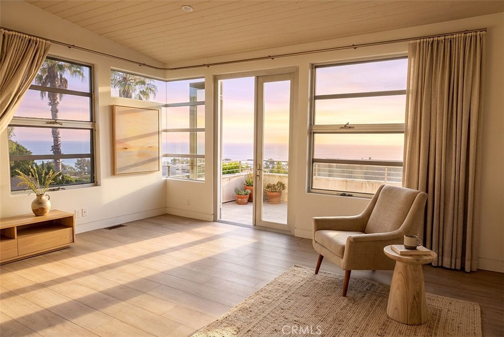 Living room with large ocean-view windows, a balcony, and a chair in warm sunset light.