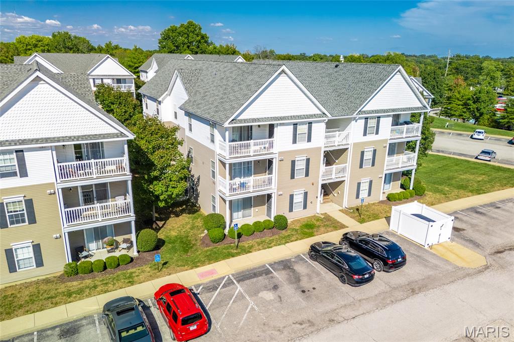 Condominium building with white balconies and gray gabled roofs beside a parking lot.