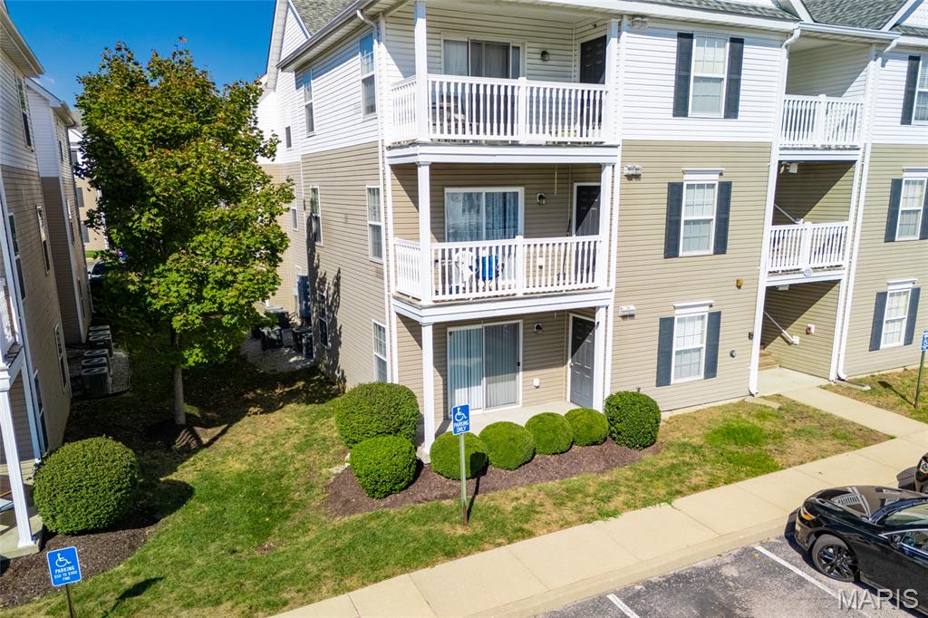 Condominium exterior with stacked white-railed balconies and landscaped shrubs beside the parking area.