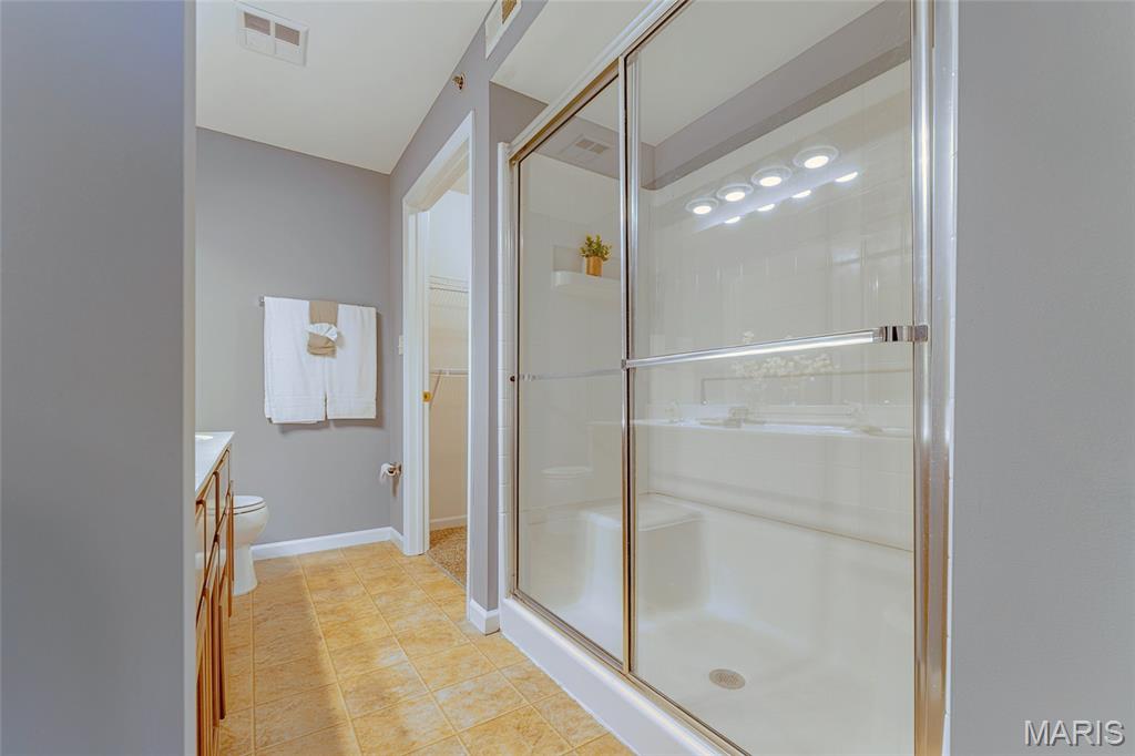 Bathroom with a large glass-enclosed shower, white tub, and warm-toned tile floor.