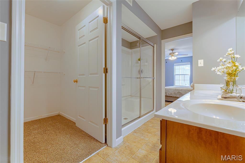 Bathroom with glass shower and white vanity, opening to a carpeted walk-in closet.