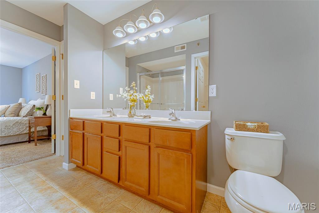 Bathroom with a long wood vanity and double sinks, with a glass shower and toilet.
