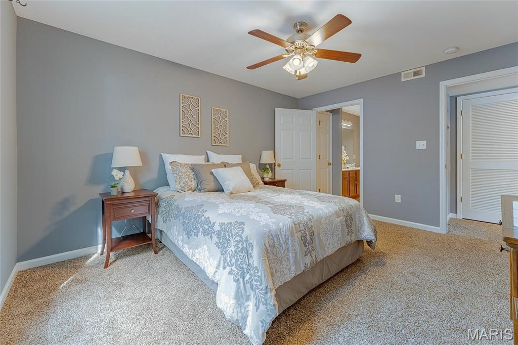 Bedroom with a floral bedspread, gray walls, beige carpet, and a wood-blade ceiling fan.