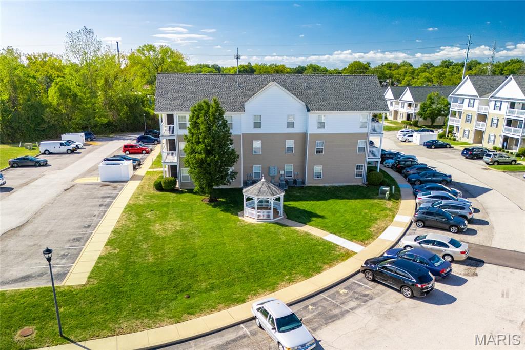 Aerial view of a condominium building with a gazebo, lawn, and surrounding parking.
