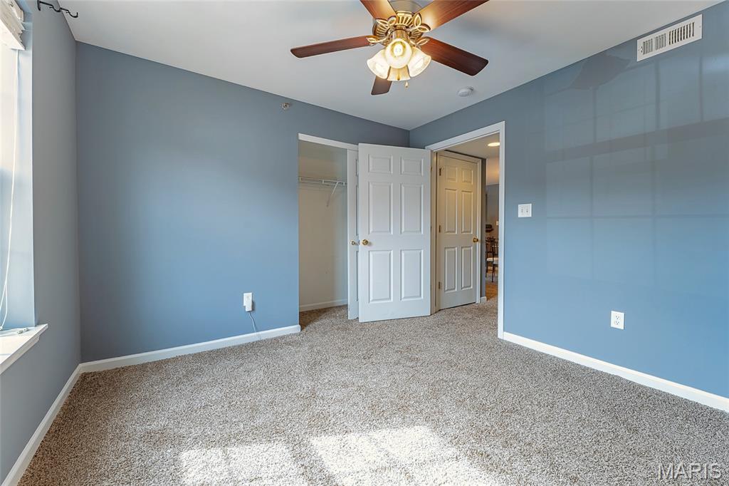 Empty bedroom with blue walls, beige carpet, ceiling fan, and open closet.