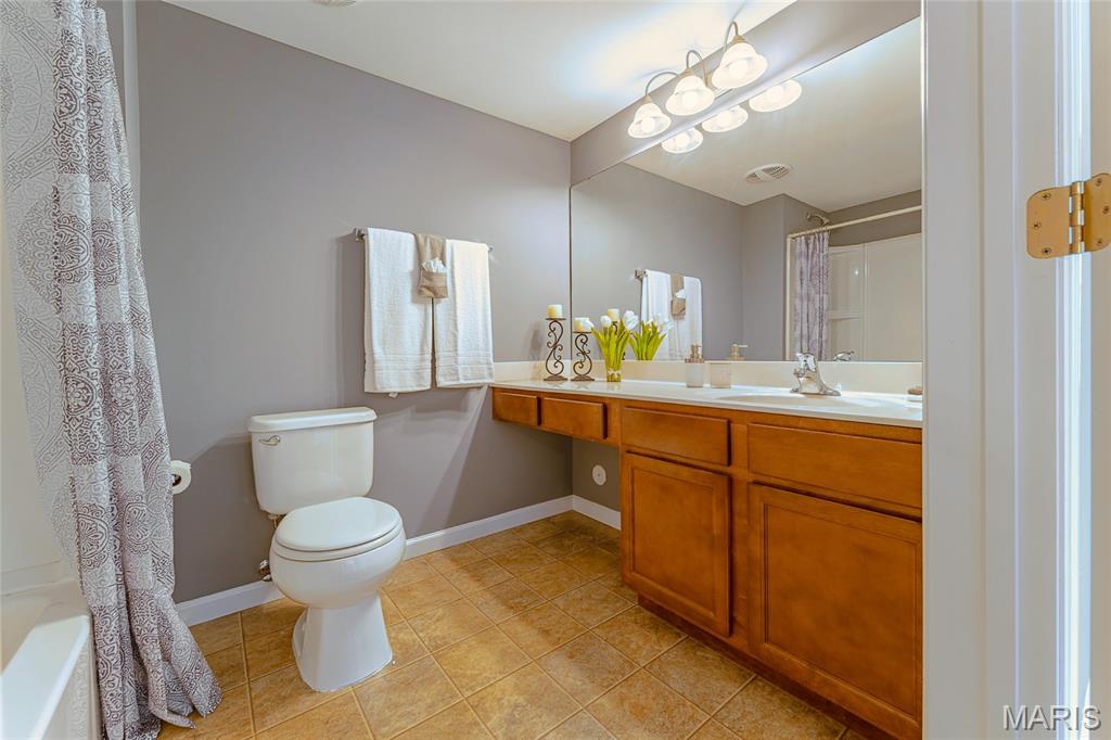 Bathroom with a long wood vanity, large mirror, and patterned shower curtain.