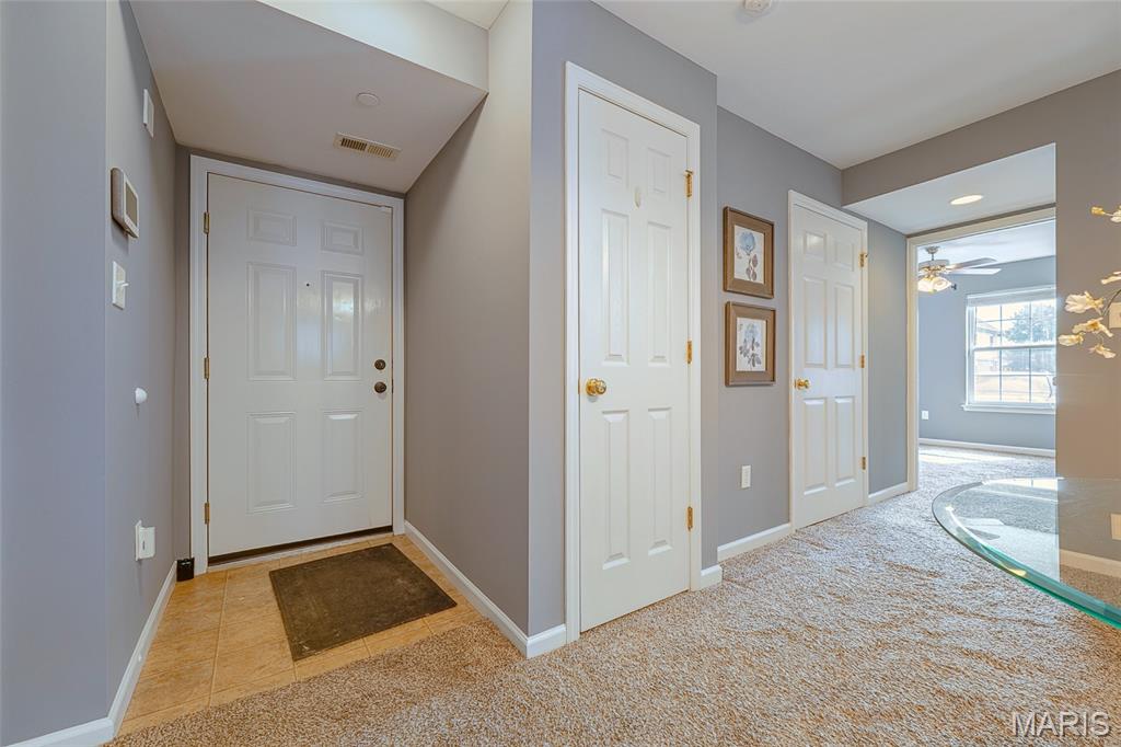 Entryway with a white front door, tiled landing, carpeted hall, and framed floral artwork.
