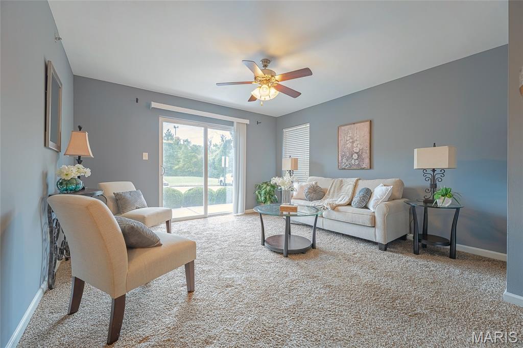 Staged living room with beige seating, a glass coffee table, and sliding doors overlooking greenery.