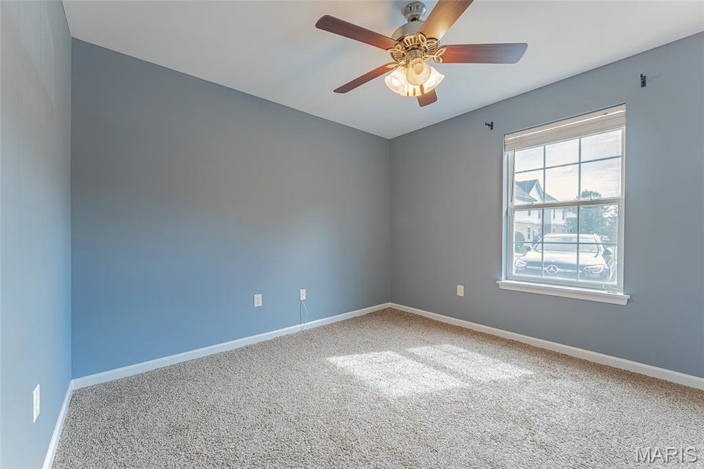 Vacant bedroom with blue-gray walls, beige carpet, ceiling fan, and a sunlit window.