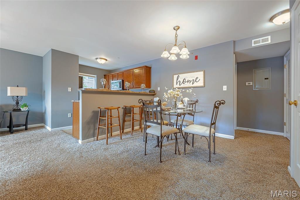 Dining area with a glass table and chairs beside a kitchen breakfast bar with wood cabinets.