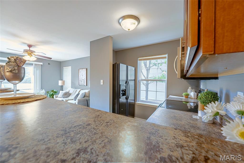 Open kitchen with a broad countertop, wood cabinets, dark refrigerator, and adjoining living room.
