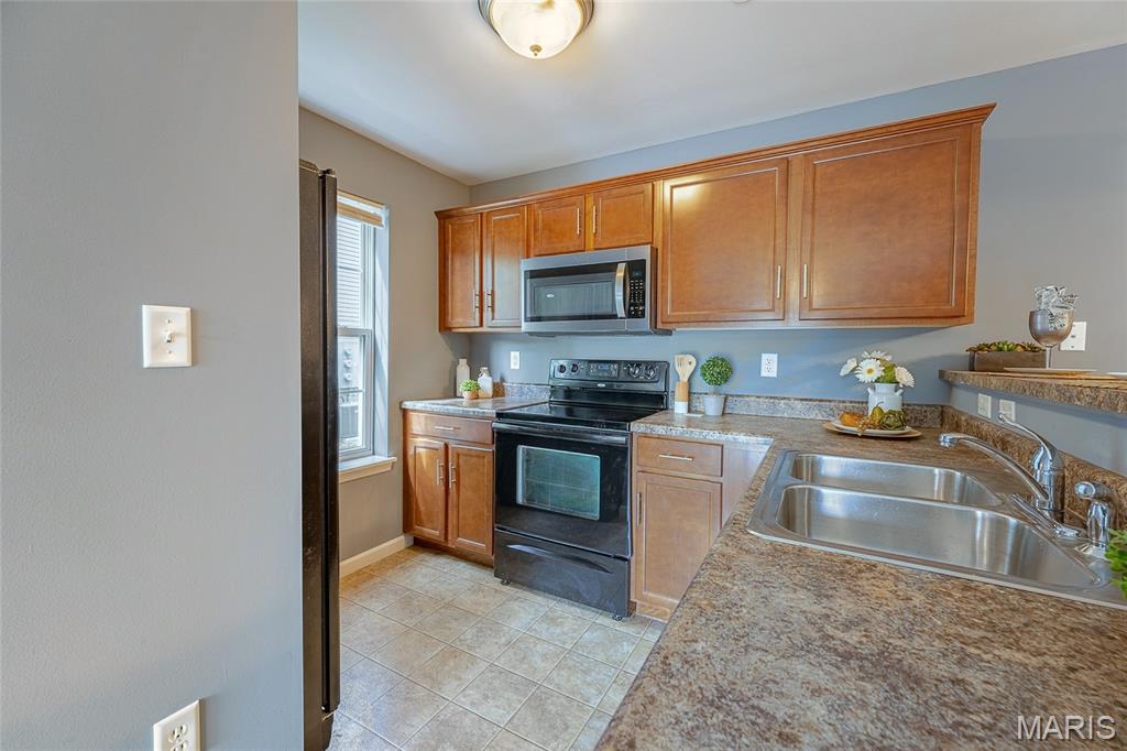 Kitchen with warm wood cabinets, black range, speckled counters, and a double-basin stainless-steel sink.