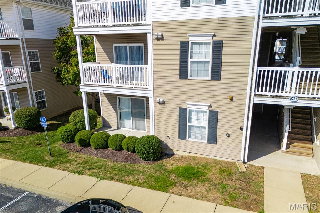 Tan condominium exterior with white-railed balconies, landscaped shrubs, and an open stairwell.