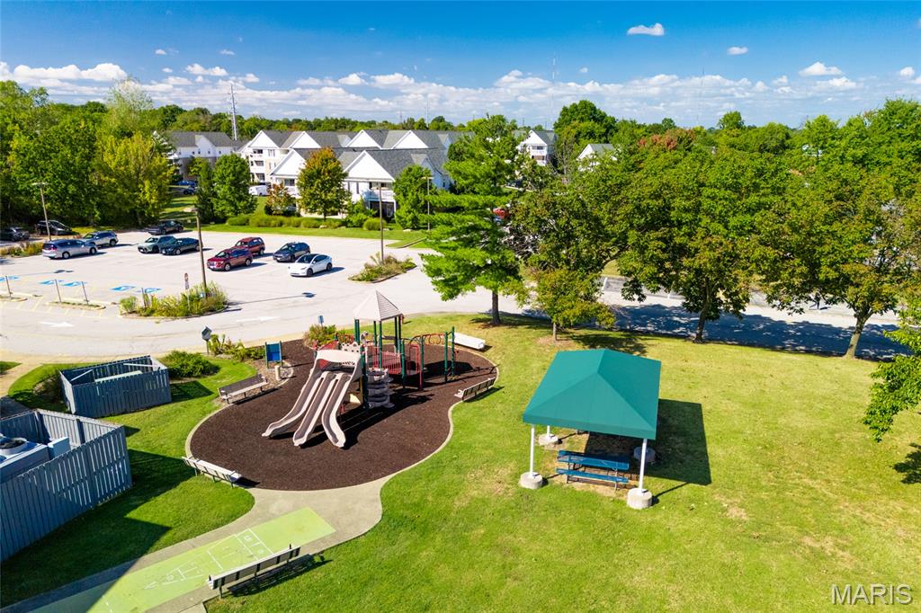 Aerial view of a community playground and covered picnic bench beside a parking lot.