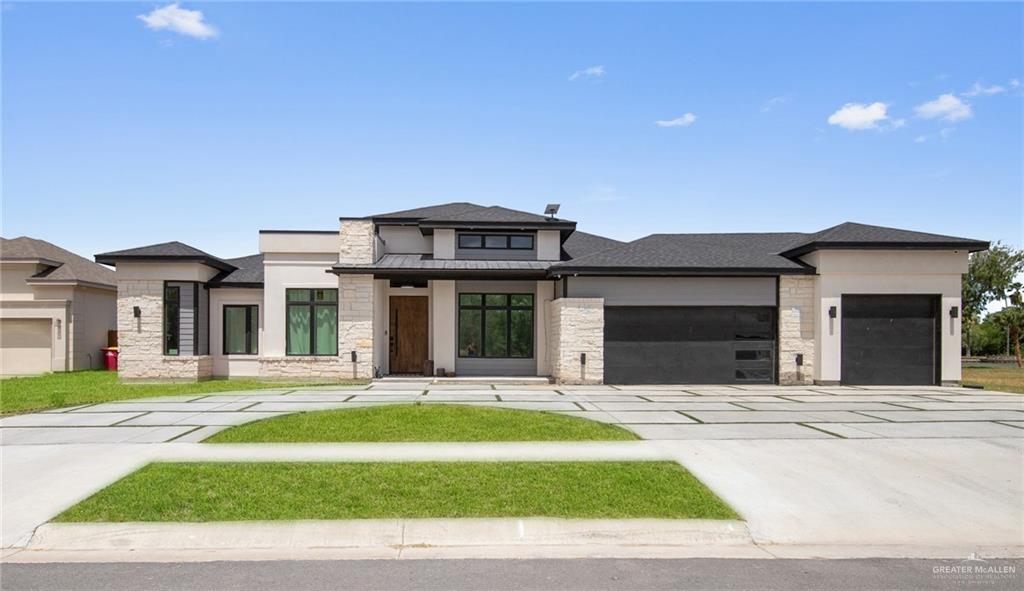 Modern single-story home with stone accents, two garage doors, and a wide segmented driveway.