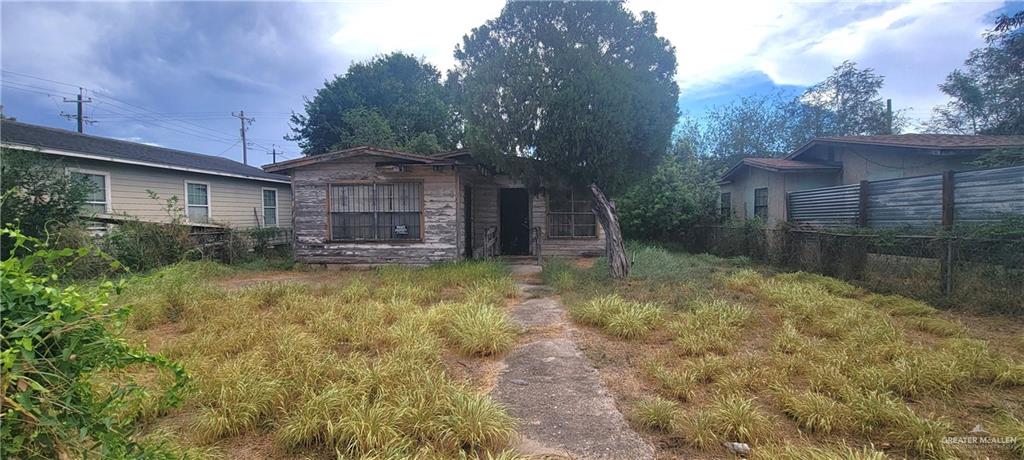 Weathered single-story house with a boarded window, overgrown yard, and concrete walkway.