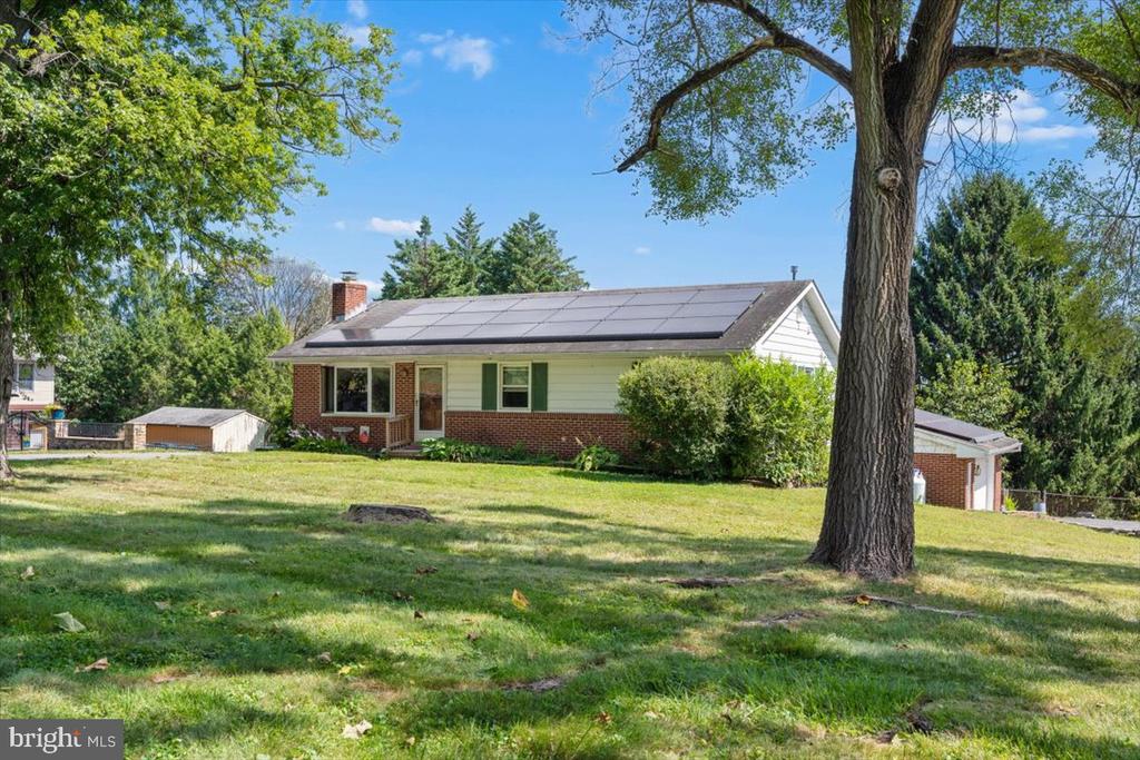 Single-story ranch home with rooftop solar panels, brick facade, and a large tree in the front yard.