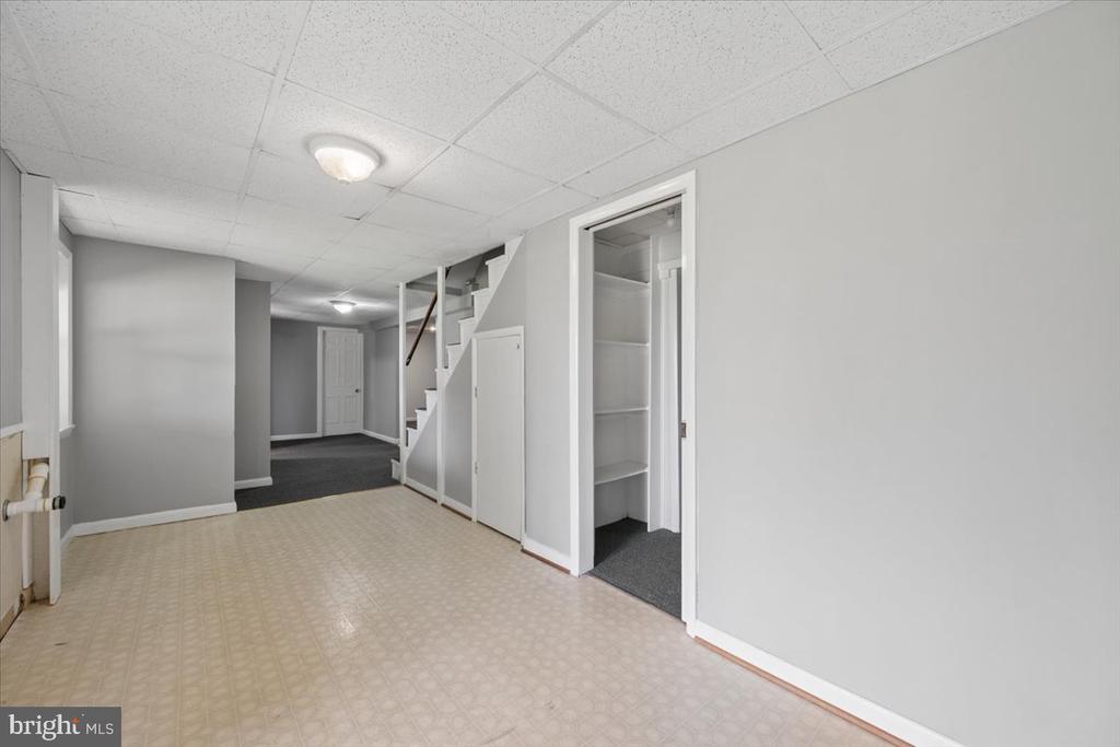 Empty lower-level room with patterned flooring, gray walls, stairs, and storage closets.