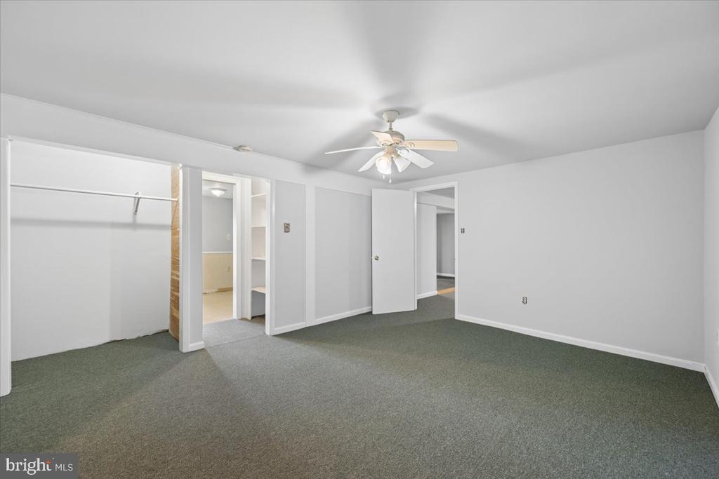 Empty bedroom with gray carpet, an open closet, and a ceiling fan with light.