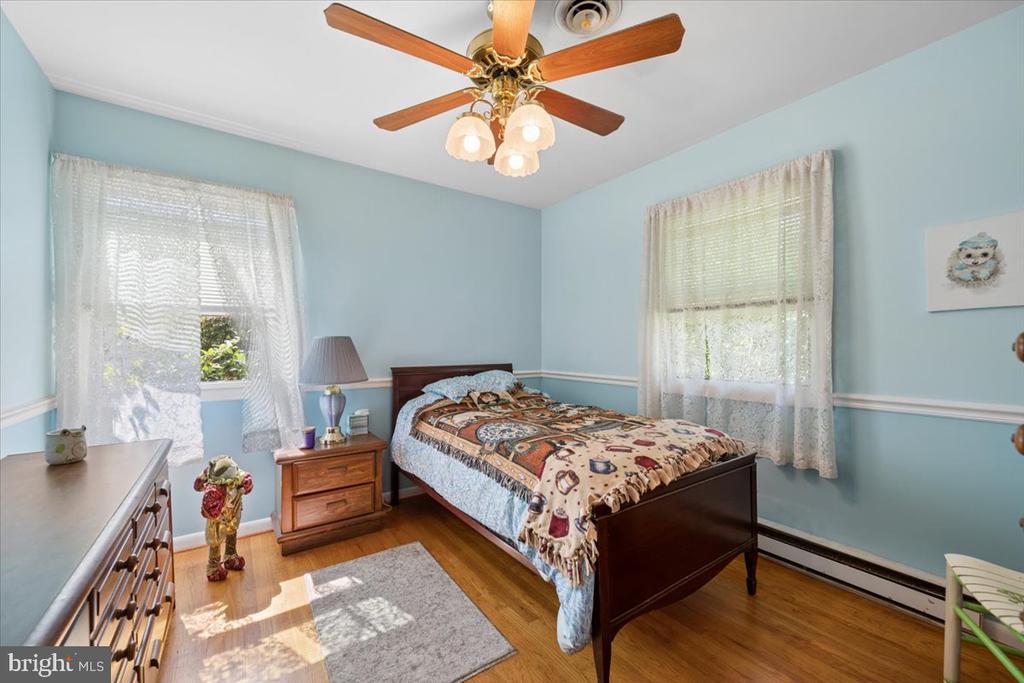 Bedroom with pale blue walls, hardwood floors, and a dark wood bed between two curtained windows.
