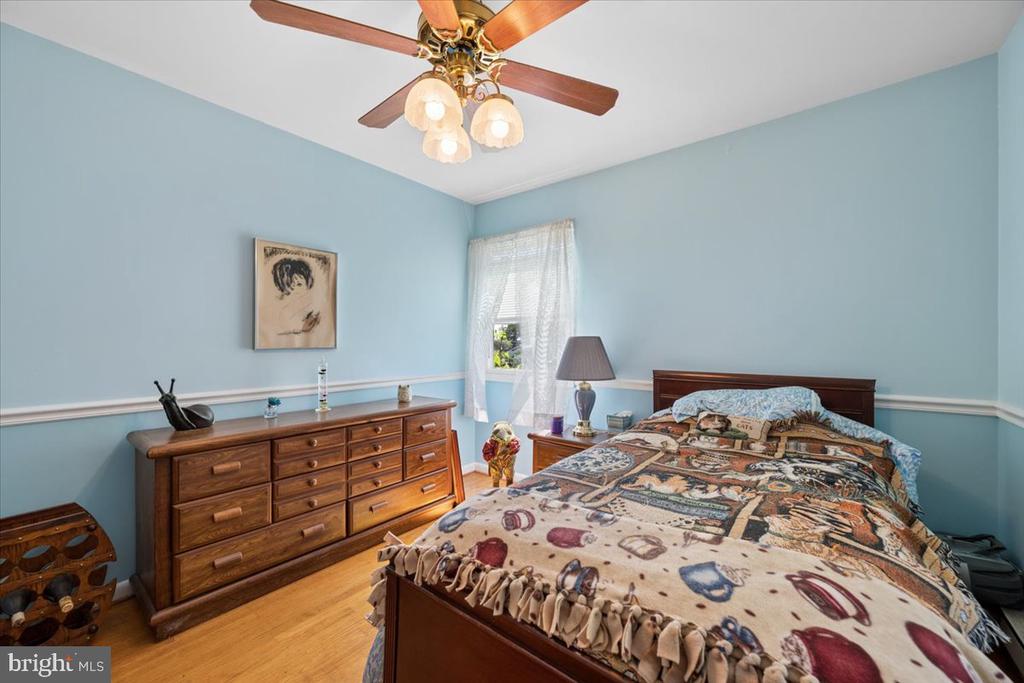 Furnished bedroom with pale blue walls, a wooden dresser, patterned bedding, and a ceiling fan.