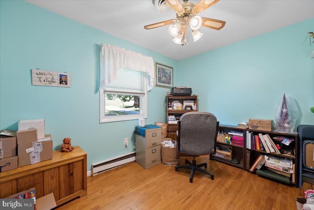 Home office with turquoise walls, wood floors, a curtained window, and a gray chair among shelves and boxes.