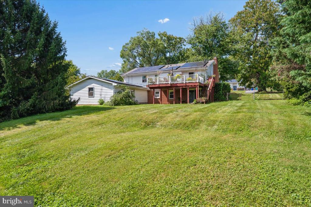 Home’s rear exterior with a raised deck, rooftop solar panels, and a broad sloping lawn.