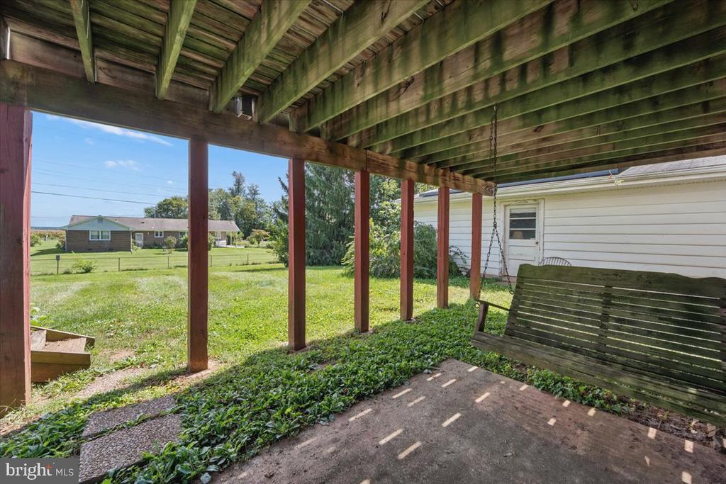 Covered patio with a hanging wooden swing bench overlooking a sunny grassy yard.