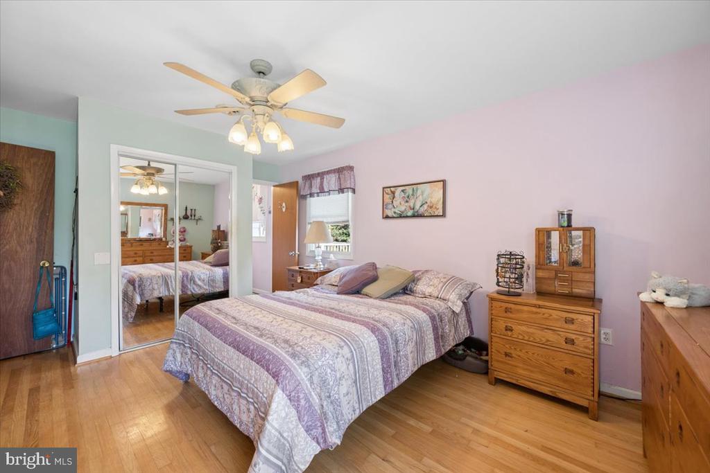 Bedroom with a patterned bedspread, mirrored closet doors, ceiling fan, and hardwood floors.