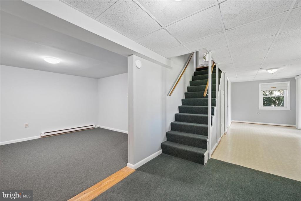 Unfurnished basement with a carpeted staircase, gray carpet, and an adjoining room with a window.