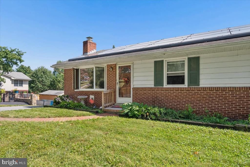 Single-story brick-and-siding home with solar panels, green shutters, and a front lawn.