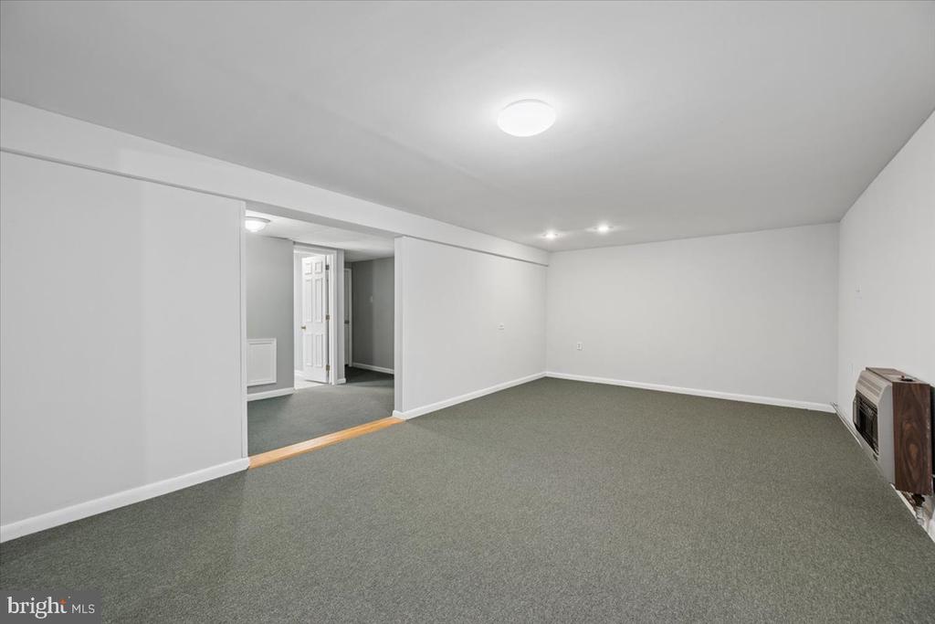 Vacant carpeted room with white walls, recessed lights, and a wall-mounted heater.