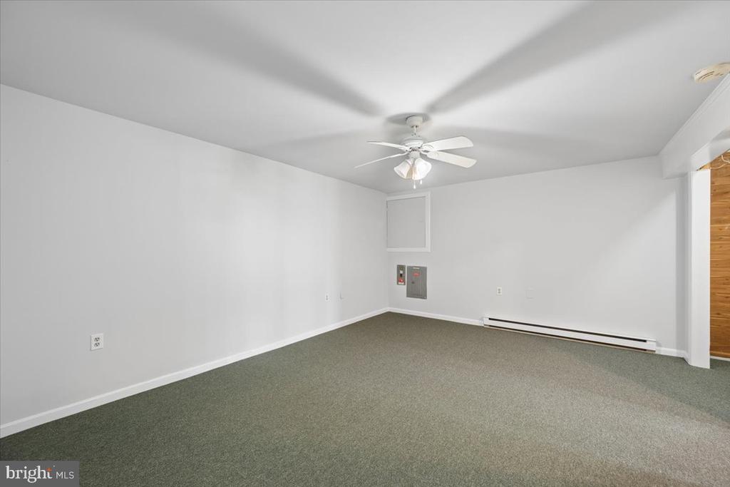 Empty carpeted room with white walls, a ceiling fan, and a baseboard heater.