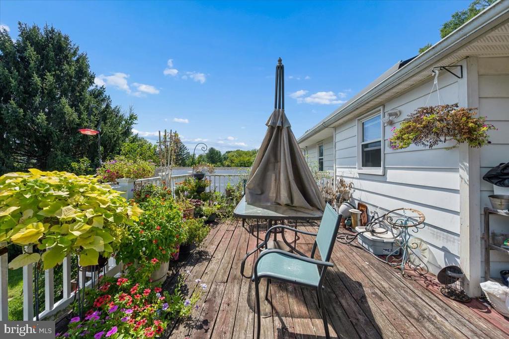Wooden deck with patio seating, a closed umbrella, and colorful potted flowers along the railing.