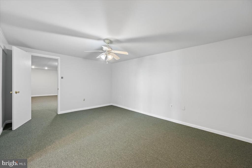 Empty carpeted room with a ceiling fan and an open doorway.