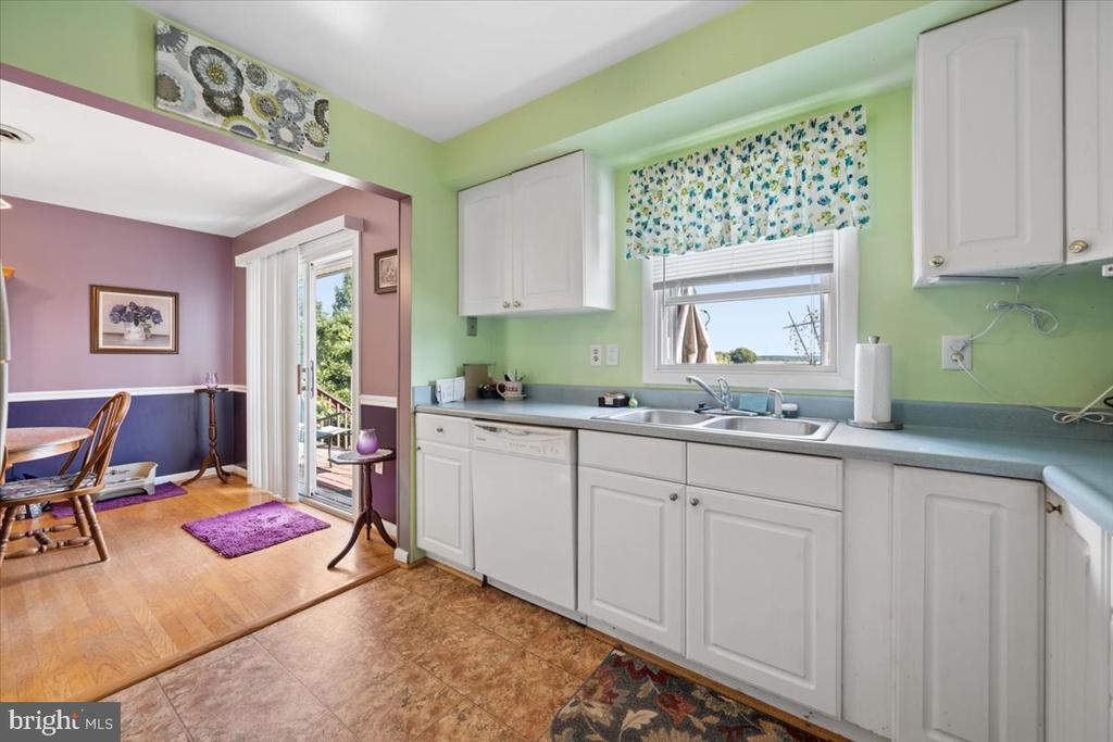Kitchen with white cabinets and gray counters, opening into a mauve dining area with a glass exterior door.